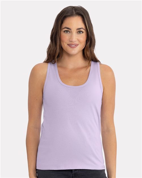 A person with long brown hair is smiling, wearing a sleeveless Next Level Women's Cotton Tank in lilac and black pants, against a plain white background.