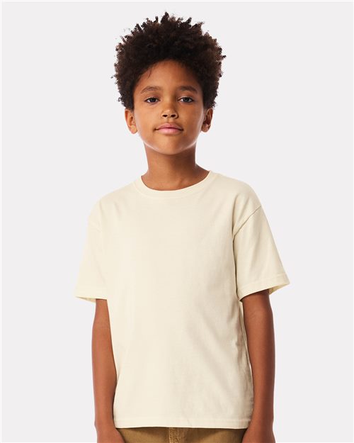 A young person with curly hair, wearing a BELLA + CANVAS Youth 6oz. Heavyweight Tee made from Airlume combed cotton, stands against a neutral background, looking at the camera.