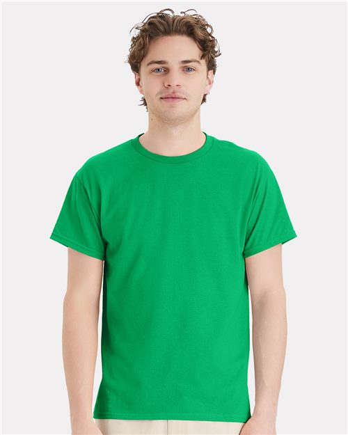 A person with short curly hair is wearing a bright green Hanes Ecosmart™ T-shirt, made from a sustainable cotton/polyester blend, and light pants, standing against a plain white background.