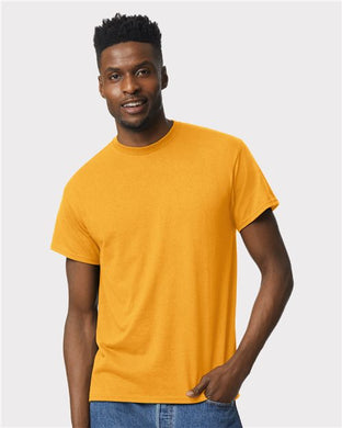 Wearing a vibrant Gildan - DryBlend® T-Shirt, crafted sustainably, and blue jeans, a person exudes OEKO-TEX certified style with a smile and one hand in their pocket against a plain white background.