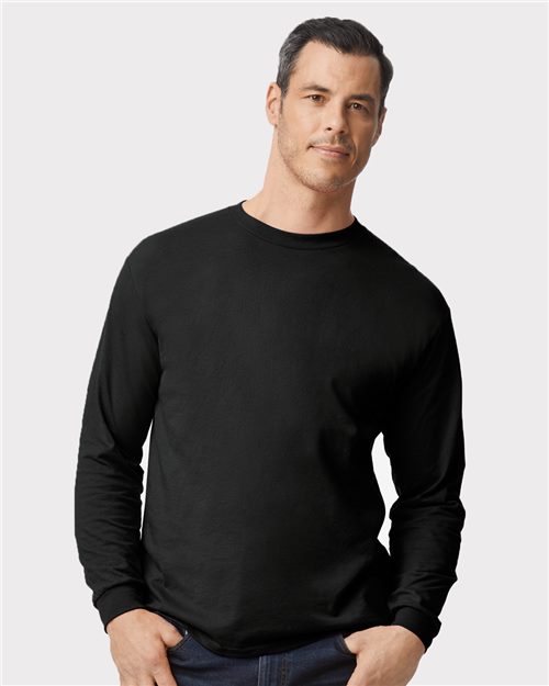 Load image into Gallery viewer, A man with short dark hair wears a plain black Gildan DryBlend® 50/50 Long Sleeve T-Shirt, produced sustainably, against a light gray background. He completes his look with dark jeans and stands relaxed, one hand in his pocket.
