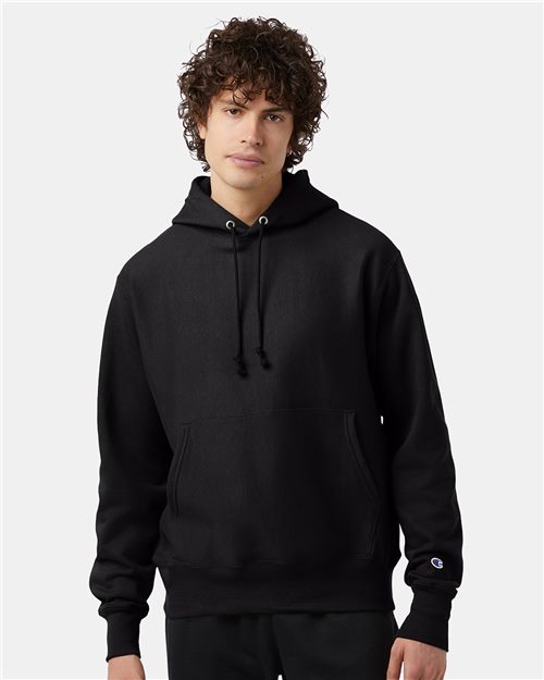 Load image into Gallery viewer, Someone wears a Champion Reverse Weave® Hooded Sweatshirt, a black hoodie with drawstrings, against a white background. The sleeve displays the embroidered Champion logo, highlighting its craftsmanship.
