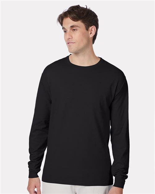 Load image into Gallery viewer, A person in a Hanes - Beefy-T® Long Sleeve T-Shirt, plain black and made from ring-spun cotton, stands against a light gray background. They look slightly to the side, with their shirt contrasting against pale pants.
