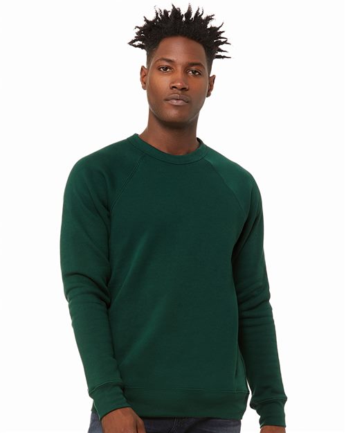 Load image into Gallery viewer, A person with short, spiked hair stands against a white background, wearing a BELLA + CANVAS dark green Sponge Fleece Raglan Crewneck Sweatshirt and dark jeans. They look directly at the camera, showcasing fashion that&#39;s both stylish and sustainable.
