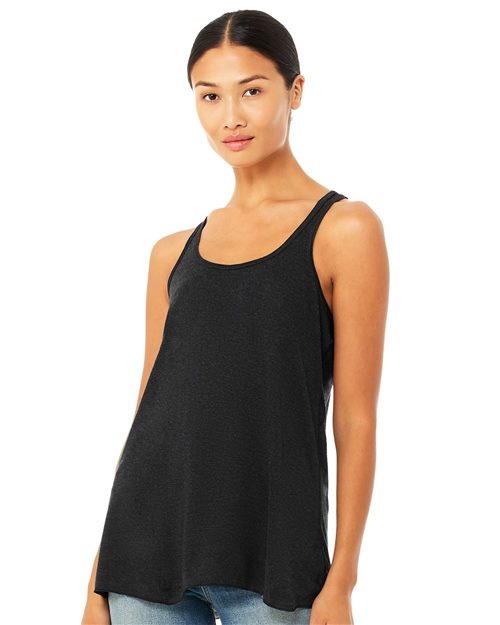 A person in a loose, black BELLA + CANVAS Women's Flowy Racerback Tank and jeans stands against a white background, looking forward with a slight smile and long dark hair tied back.