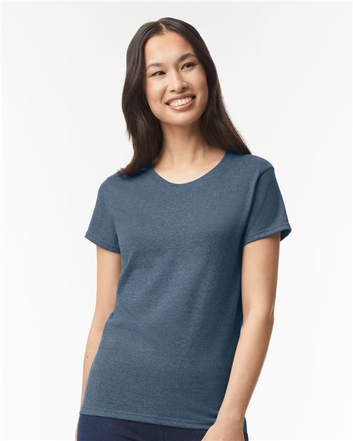 A woman with long dark hair smiles at the camera, wearing a plain blue Gildan - Heavy Cotton™ Women’s T-Shirt and dark pants against a white background.