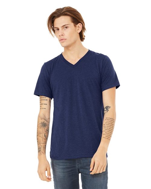 A person with brown hair wears a navy BELLA + CANVAS Triblend V-Neck Short Sleeve Tee and jeans, displaying tattooed arms against a plain white backdrop.