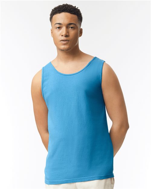 A person in a Comfort Colors Garment-Dyed Heavyweight Tank Top, blue, and beige pants stands against a plain white background, embodying sustainable manufacturing. Each outfit is stylish and responsibly crafted.