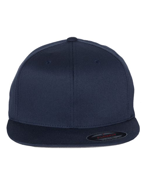 The Flexfit Pro-Baseball On Field Cap, in navy blue, features a high-profile flatbill design with a central seam from brim to crown. Made from a polyester cotton blend, it has a structured build and includes a small sticker on the brim front.