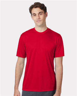 A person in a Hanes - Cool DRI® Performance T-Shirt, made from moisture-management polyester interlock, and dark pants stands in front of a light gray backdrop. They have short, dark hair and a neutral expression, with arms resting at their sides.