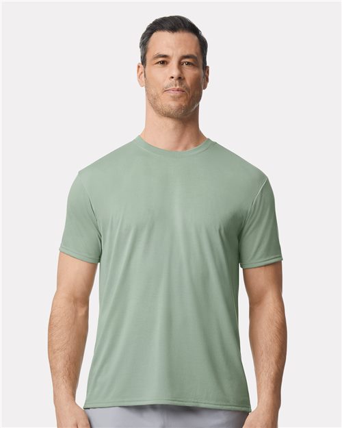 A person stands against a white background wearing a Gildan - Performance® T-Shirt by Gildan in light green. The sustainably crafted, short-sleeved design complements their straightforward gaze.