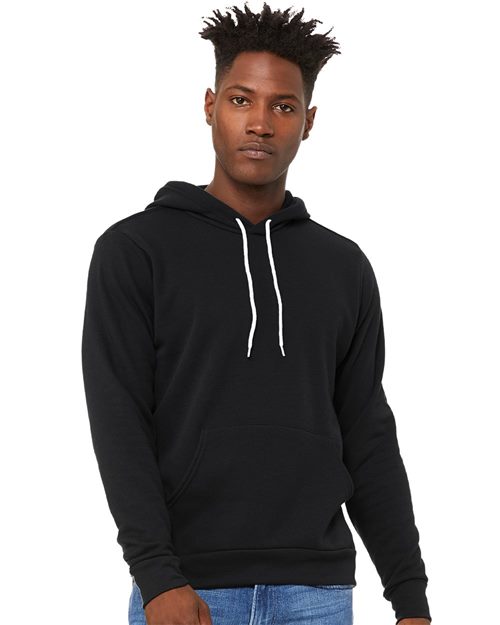 A person in a black BELLA + CANVAS Sponge Fleece Hoodie, made from Airlume combed and ring-spun cotton, stands against a white background with styled short hair, wearing blue jeans and showcasing unisex sizing with effortless style.