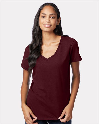 A long-haired person wearing a maroon Hanes Perfect-T Women’s V-Neck T-Shirt made from ring-spun cotton and jeans stands against a plain light gray background, appearing relaxed with their arms at their sides.