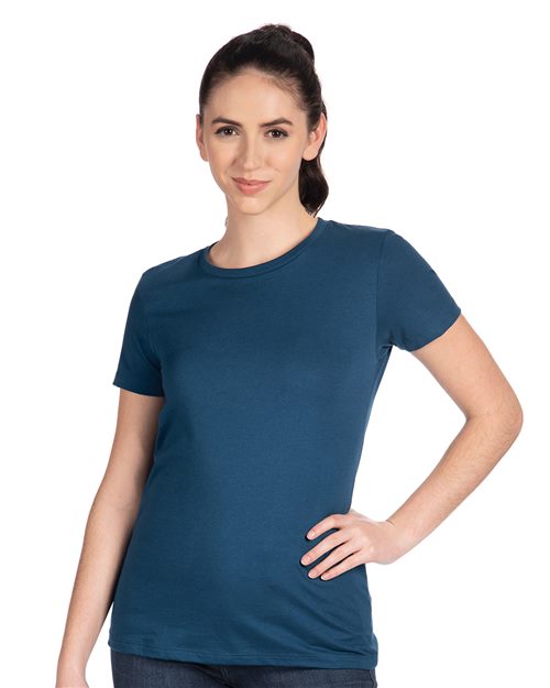 Load image into Gallery viewer, A person with dark hair, tied back, is wearing the Next Level - Women’s Cotton T-Shirt in dark blue combed ring-spun cotton. They are standing and smiling with one hand on their hip against a plain white background.
