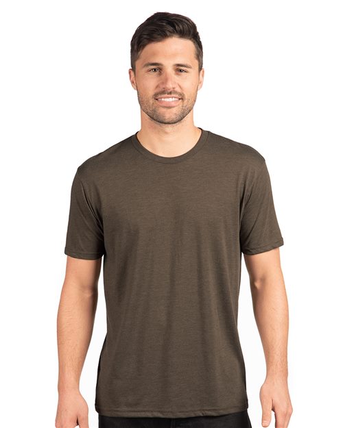 Wearing a Next Level - Triblend T-Shirt, a person with short dark hair smiles against a plain white background, embodying effortless sustainable style.