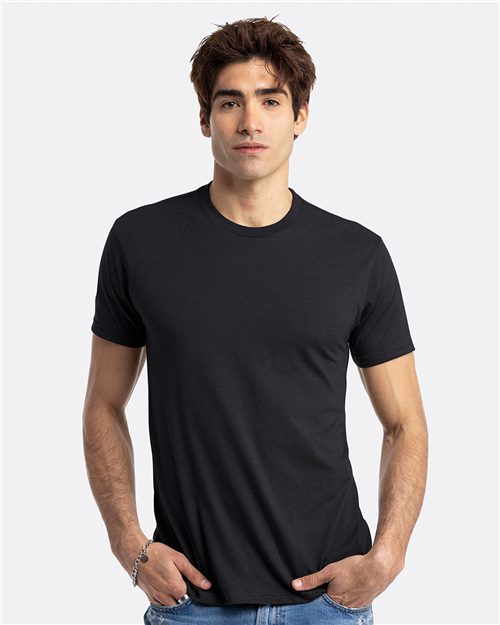 Load image into Gallery viewer, A person with short brown hair wears a plain black Next Level - CVC T-Shirt and blue jeans, standing against a plain white background with hands in pockets.
