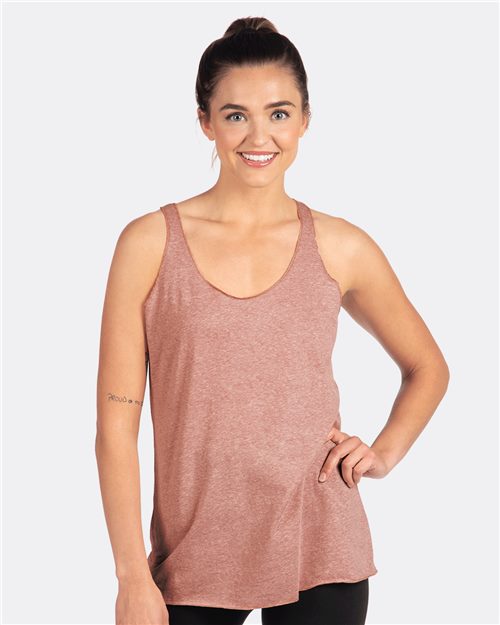 Load image into Gallery viewer, Wearing a Next Level Women&#39;s Triblend Racerback Tank in pink and black pants, this person exudes confidence with a smile and hand on their hip against a white backdrop. Made from polyester/combed ring-spun cotton/rayon blend, the outfit showcases socially conscious manufacturing.
