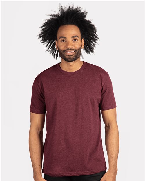 A smiling person wears a maroon Next Level Sueded T-Shirt with black pants against a white background. Their hair is natural and voluminous, embodying comfort and style through socially conscious manufacturing.