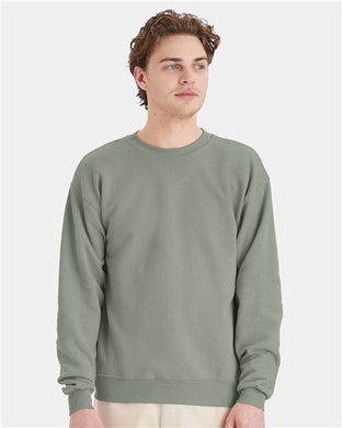 A person wearing a Hanes - Ecosmart® Crewneck Sweatshirt in light green gazes to the side against a white background. Their short, wavy hair frames their neutral expression, embodying the brand's commitment to sustainable manufacturing.