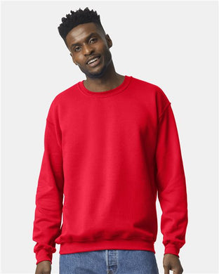 A man smiles wearing a Gildan - Heavy Blend™ Crewneck Sweatshirt in red and blue jeans against a light gray backdrop.