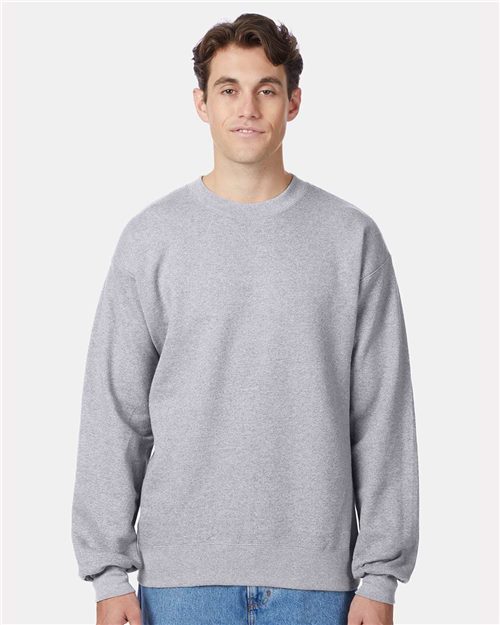 A person in a Hanes Ultimate Cotton® Crewneck Sweatshirt and blue jeans, both crafted through socially conscious manufacturing, stands against a plain white background.