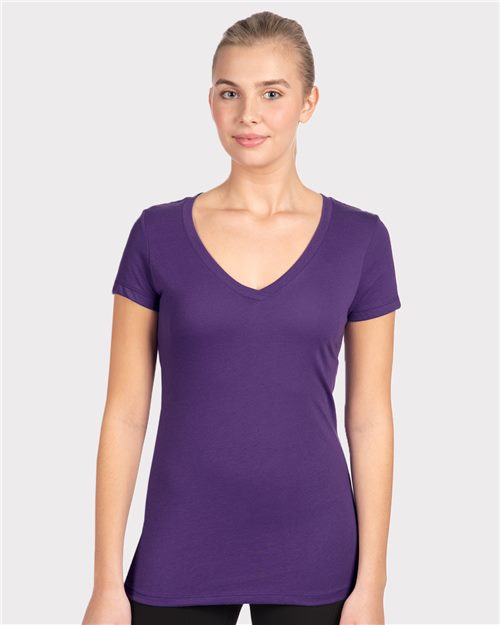 Load image into Gallery viewer, A person with their hair pulled back, wearing a Next Level Women&#39;s Ideal V-Neck T-Shirt in purple and black pants, stands against a plain gray background, smiling at the camera.
