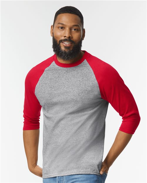 Load image into Gallery viewer, A bearded man smiles in a Gildan Heavy Cotton™ Raglan Three-Quarter Sleeve T-Shirt, featuring gray and red colors. With short hair, he stands against a plain white background, enjoying the comfort and quality of sustainable manufacturing.
