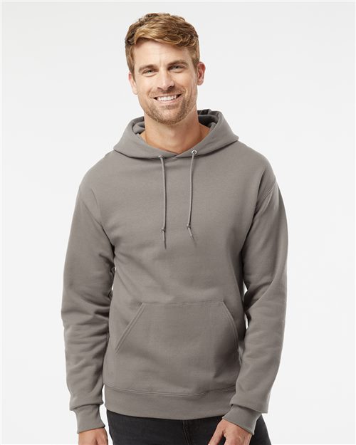 Load image into Gallery viewer, A smiling man wears the JERZEES - NuBlend® Hooded Sweatshirt, made from pill-resistant fleece with a front pocket and drawstrings, against a plain white background, highlighting socially conscious manufacturing.
