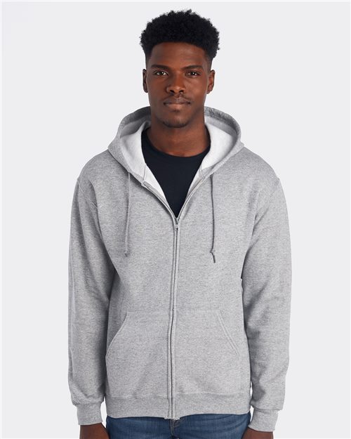 Load image into Gallery viewer, A man in a JERZEES - NuBlend® Full-Zip Hooded Sweatshirt made with sustainably sourced cotton pairs it with a black t-shirt and blue jeans, standing against a plain white background.
