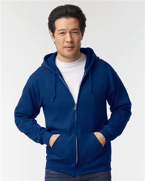 Load image into Gallery viewer, A person in a white t-shirt and a blue Gildan - Heavy Blend™ Full-Zip Hooded Sweatshirt stands with hands in pockets against a plain background.
