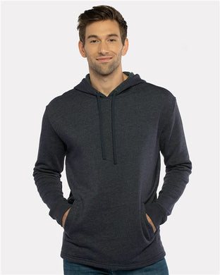 A person in a Next Level - Malibu Welt Pocket Hoodie, made from dark gray cotton/polyester fleece with a drawstring and tear-away label, stands against a white background. Manufactured socially consciously, they have short brown hair and wear a slight smile with their hands in the front pocket.