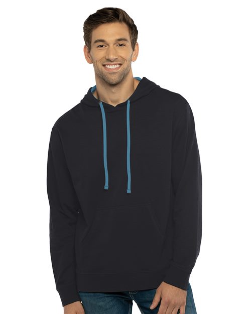 A person in a black Next Level Laguna Hoodie, made from cozy French terry fleece, with blue drawstrings and jeans, smiles at the camera. The hoodie includes a tear-away label and front pocket. The background is plain white.