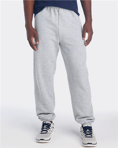 Load image into Gallery viewer, A person in a navy shirt, gray JERZEES - NuBlend® Sweatpants, and running shoes stands against a plain white background, showing only the lower half of the body.
