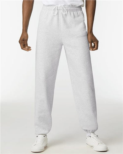 Someone wearing Gildan Heavy Blend™ Sweatpants, crafted from OEKO-TEX certified fabric with an elastic waistband and cuffs, poses against a plain background. White sneakers complement the look, and a white top at the waist underscores sustainable manufacturing practices.