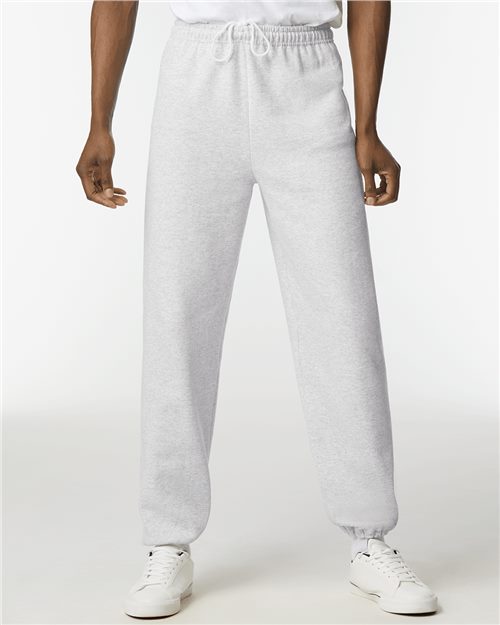 Someone wearing Gildan Heavy Blend™ Sweatpants, crafted from OEKO-TEX certified fabric with an elastic waistband and cuffs, poses against a plain background. White sneakers complement the look, and a white top at the waist underscores sustainable manufacturing practices.