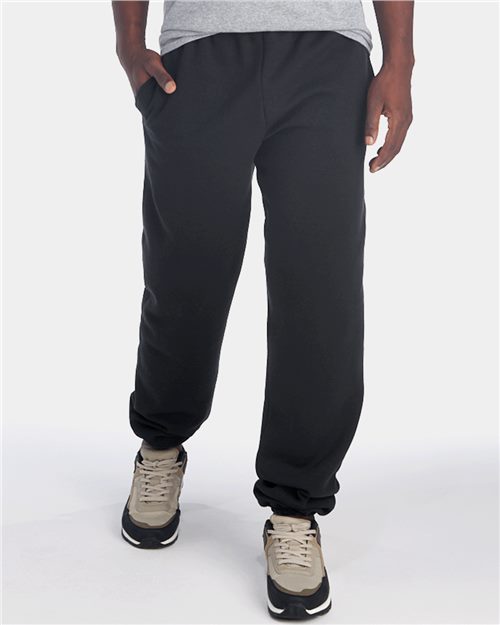 Load image into Gallery viewer, A person against a white background wears JERZEES Super Sweats NuBlend® Sweatpants with Pockets in black and gray sneakers, casually resting one hand in their pocket.
