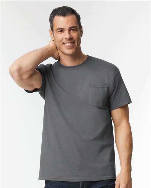 Load image into Gallery viewer, A person smiles while wearing a gray Gildan Heavy Cotton™ Pocket T-Shirt, with one hand touching the back of their neck against a plain white background.
