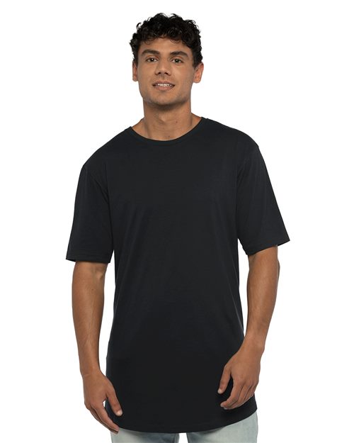 Load image into Gallery viewer, A person in a plain black Next Level Cotton Long Body T-Shirt, made of combed ring-spun cotton, and light-colored pants stands against a white background, slightly smiling with one hand by their side and the other in front.
