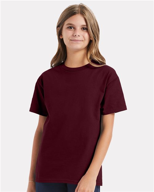 Load image into Gallery viewer, A young person with long hair stands against a white background, gently smiling while wearing a plain maroon Hanes - Authentic Youth T-Shirt made of 100% cotton jersey.
