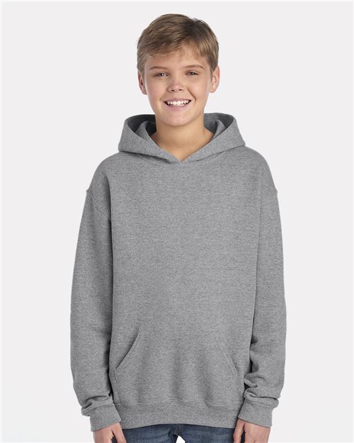 Load image into Gallery viewer, A young boy wearing a JERZEES - NuBlend® Youth Hooded Sweatshirt smiles at the camera with hands casually in the pouch pocket. Made from pill-resistant fleece, this gray hoodie is set against a plain light gray background and is produced through sustainable practices.
