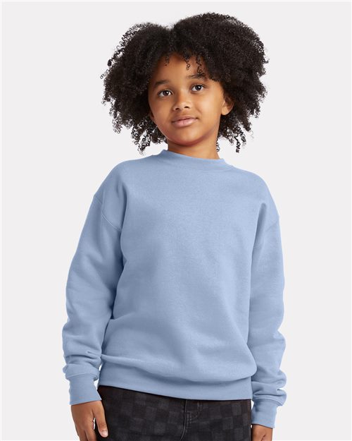 A young child with curly hair stands against a plain background, wearing a Hanes Ecosmart® Youth Crewneck Sweatshirt made from CiCLO® polyester. Their neutral expression gazes slightly to the side, reflecting sustainable manufacturing principles for a better future.