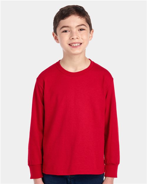 Load image into Gallery viewer, A smiling child wears a JERZEES - Dri-Power® Youth Long Sleeve 50/50 T-Shirt, crafted sustainably, against a light gray background.
