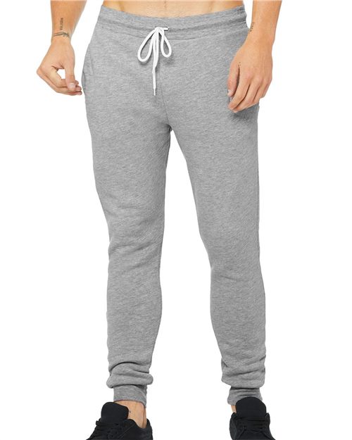 Someone is wearing BELLA + CANVAS Sponge Fleece Jogger Sweatpants in light gray, made from Airlume combed cotton with a white drawstring against a white background. The black shoes create contrast. These unisex joggers offer a perfect fit and are produced sustainably.