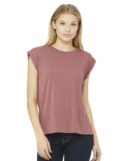 A person with long, blonde hair wears a BELLA + CANVAS Women's Flowy Rolled Cuffs Muscle Tee in mauve and dark pants, looking directly at the camera against a plain white background. The attire is crafted through sustainable manufacturing processes.