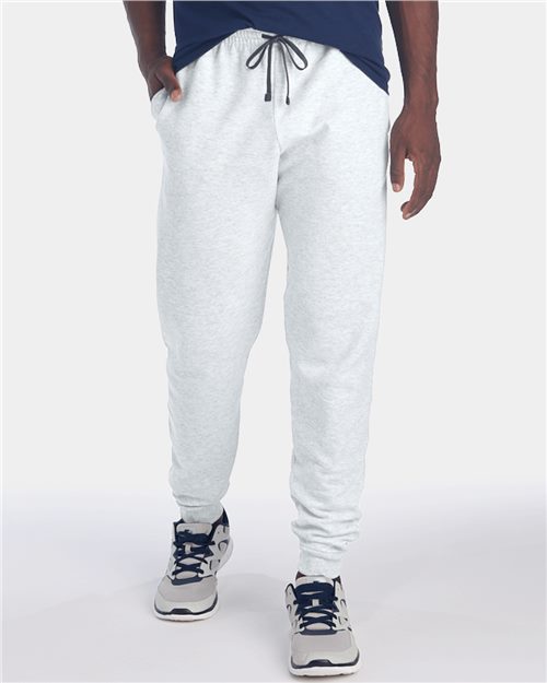 Load image into Gallery viewer, A person stands with hands in pockets, wearing JERZEES Nublend® Joggers in pill-resistant light gray fleece and white sneakers with navy accents. The dark navy shirt completes the outfit, visible only from the waist down against a plain background.
