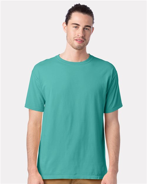 Load image into Gallery viewer, A person with long hair in a bun, wearing a teal ComfortWash by Hanes Garment-Dyed T-Shirt made of ring-spun cotton and beige pants, stands against a plain light background. They have a neutral expression and gaze directly at the camera.
