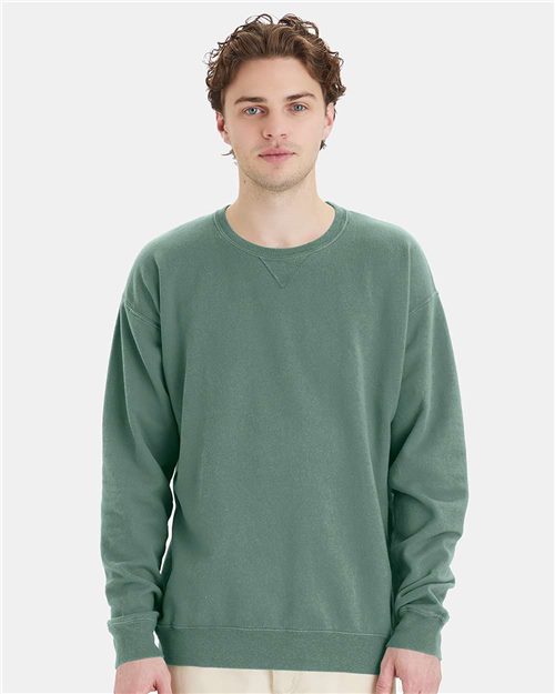 Load image into Gallery viewer, A person with short curly hair is wearing a green ComfortWash by Hanes Garment-Dyed Crewneck Sweatshirt and beige pants, standing against a light gray background.
