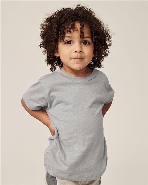 A curly-haired child wears a gray BELLA + CANVAS Toddler Triblend Tee against a neutral background, smiling slightly with hands behind their back, reflecting the comfort and sustainability of Blue Sign certified apparel.