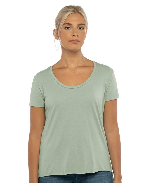 A person with long blonde hair is wearing a light green Next Level - Women's Festival Scoop Neck T-Shirt and blue jeans, standing against a white background.