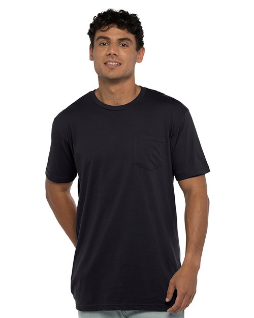 Load image into Gallery viewer, A man with short, curly hair and a smile stands against a white background wearing the Next Level - Cotton Pocket T-Shirt. The dark navy blue shirt is crafted from soft combed ring-spun cotton and features a chest pocket, with his hands behind his back.
